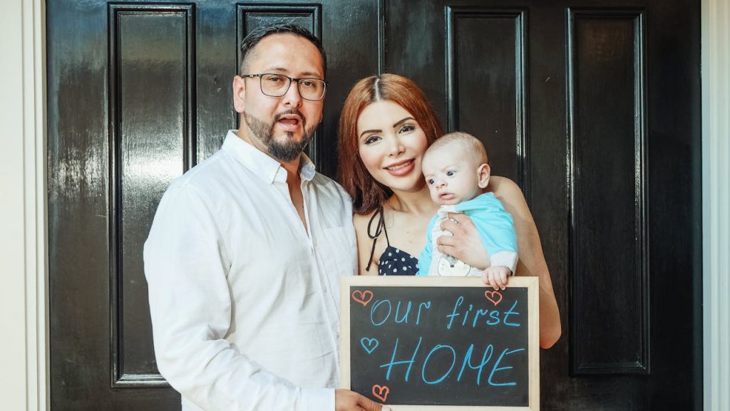 man-in-white-dress-shirt-holding-girl-in-white-dress-7578982 A joyful family stands at their new homes entrance holding a our first home sign.