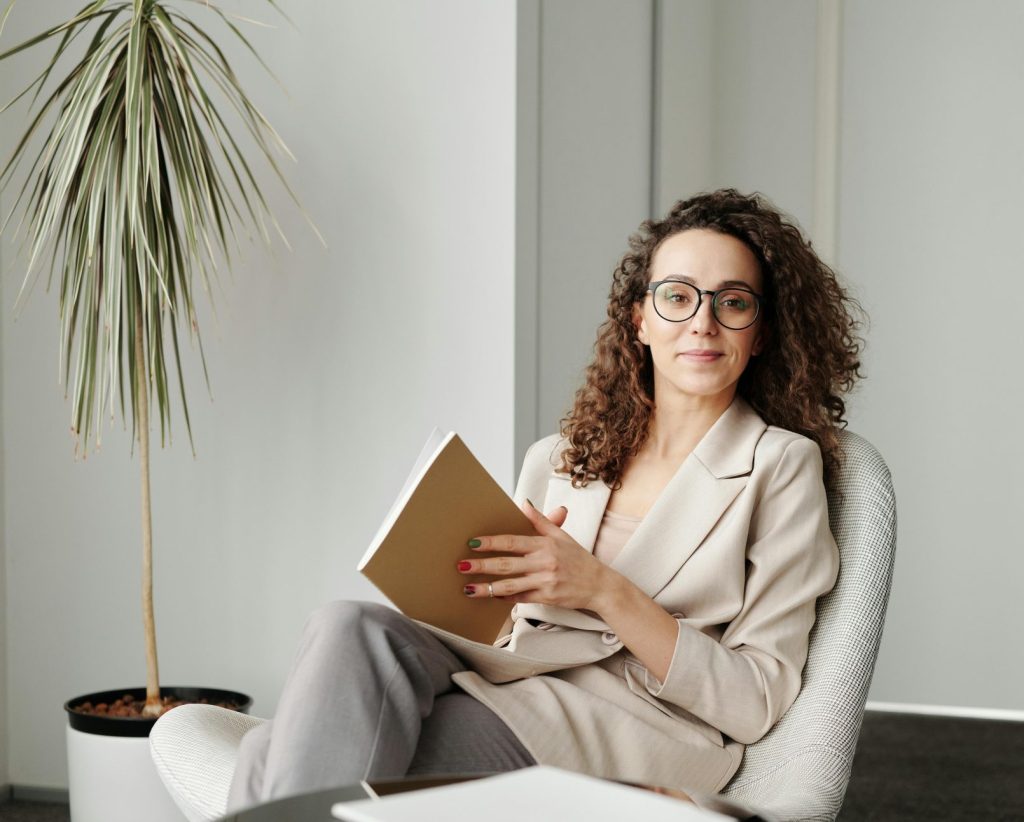 Businesswoman sitting in a modern office with a notebook, exuding professionalism and confidence.